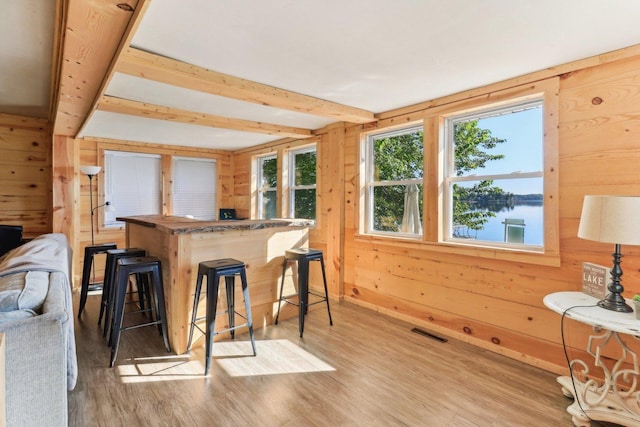 kitchen featuring wood walls, light wood-type flooring, a kitchen bar, a water view, and beam ceiling