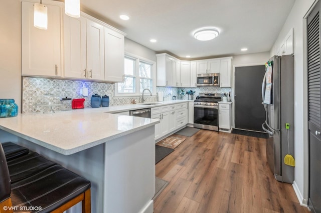 kitchen featuring dark wood-style floors, stainless steel appliances, white cabinets, a sink, and a peninsula