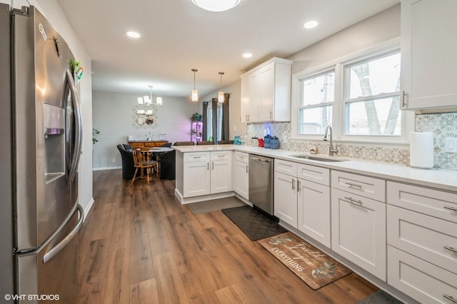 kitchen featuring decorative backsplash, white cabinets, a peninsula, stainless steel appliances, and a sink