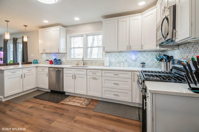 kitchen with white cabinets, appliances with stainless steel finishes, dark wood-style flooring, a peninsula, and a sink