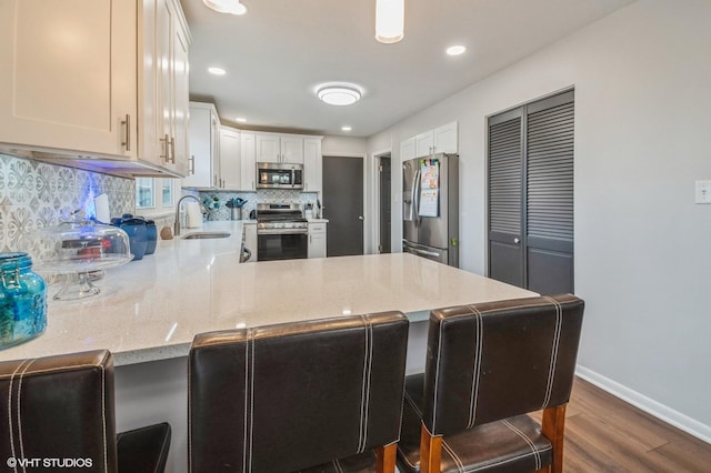 kitchen with stainless steel appliances, tasteful backsplash, a sink, a peninsula, and a kitchen breakfast bar