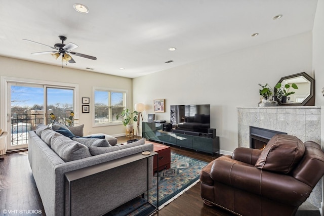 living room with visible vents, baseboards, a tiled fireplace, dark wood-type flooring, and recessed lighting