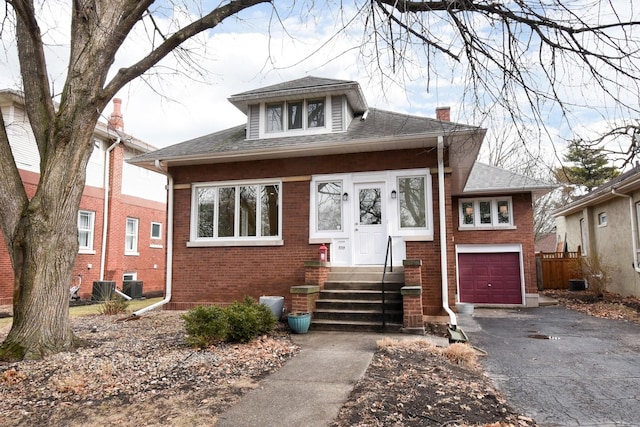 bungalow-style house with entry steps, a shingled roof, a chimney, aphalt driveway, and brick siding