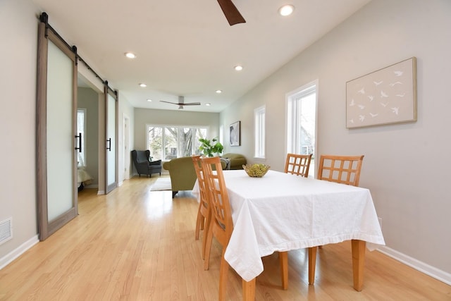 dining room with ceiling fan, a barn door, light wood-style flooring, and recessed lighting