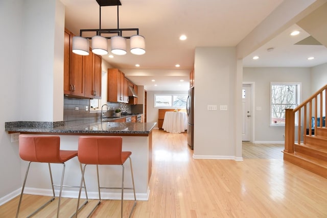 kitchen featuring decorative backsplash, brown cabinets, freestanding refrigerator, light wood-style floors, and a sink