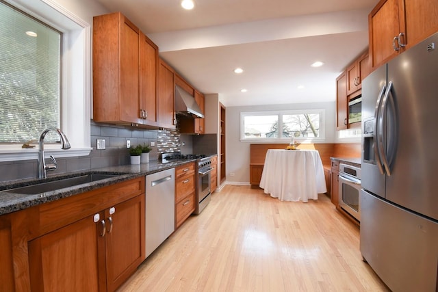 kitchen featuring brown cabinets, wall chimney range hood, stainless steel appliances, and a sink