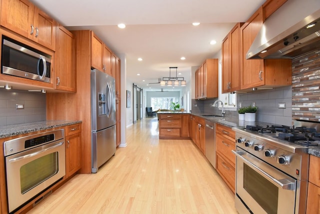 kitchen featuring wall chimney range hood, a sink, appliances with stainless steel finishes, and brown cabinets