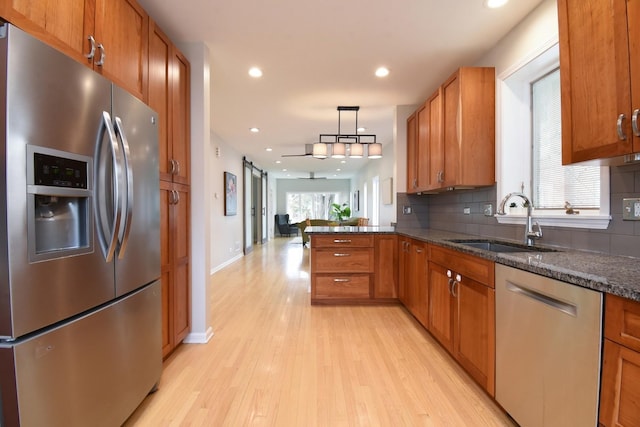 kitchen with a barn door, brown cabinetry, decorative backsplash, stainless steel appliances, and a sink