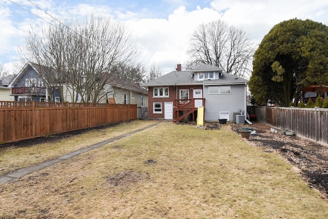 rear view of property with central air condition unit, a fenced backyard, a chimney, and a lawn