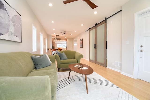 living room featuring a barn door, visible vents, ceiling fan, light wood-type flooring, and recessed lighting