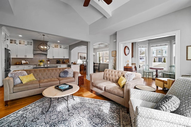 living room featuring beam ceiling, hardwood / wood-style flooring, ceiling fan with notable chandelier, and high vaulted ceiling