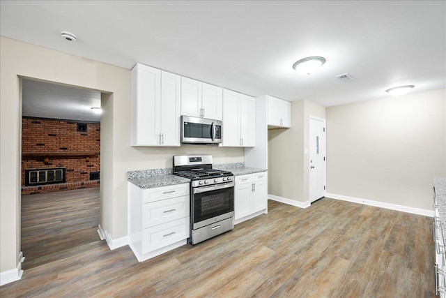 kitchen featuring appliances with stainless steel finishes, light stone countertops, light wood-type flooring, and white cabinets