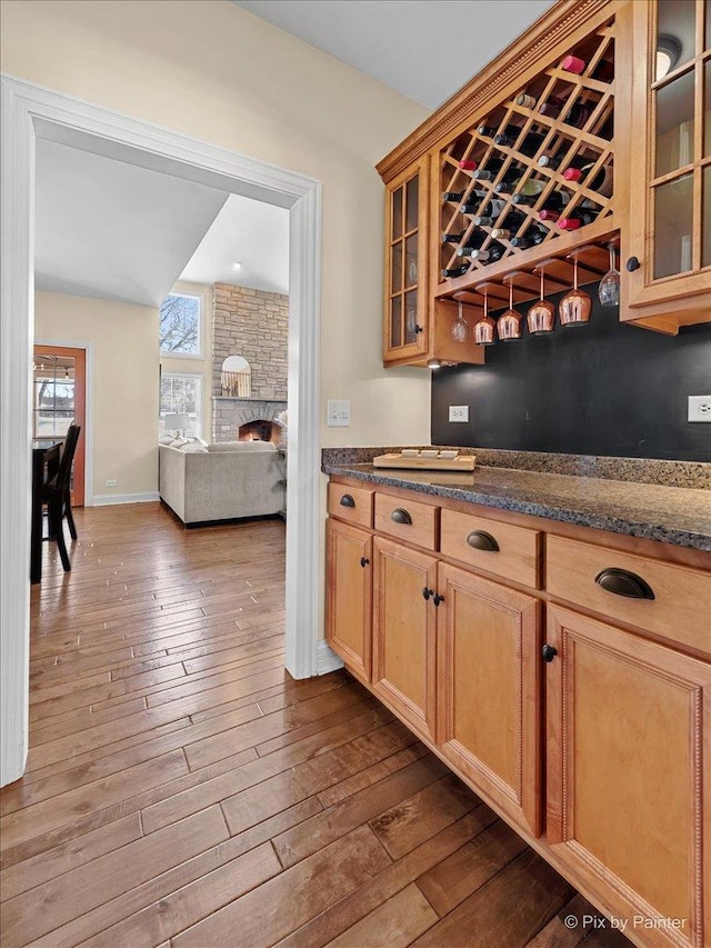 bar featuring a bar, dark wood finished floors, a stone fireplace, and baseboards