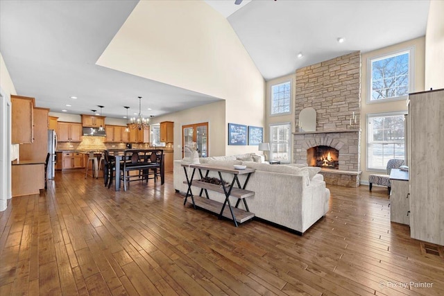 living room with a towering ceiling, an inviting chandelier, a fireplace, and dark wood finished floors