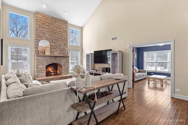 living room featuring high vaulted ceiling, dark wood-type flooring, a fireplace, visible vents, and baseboards