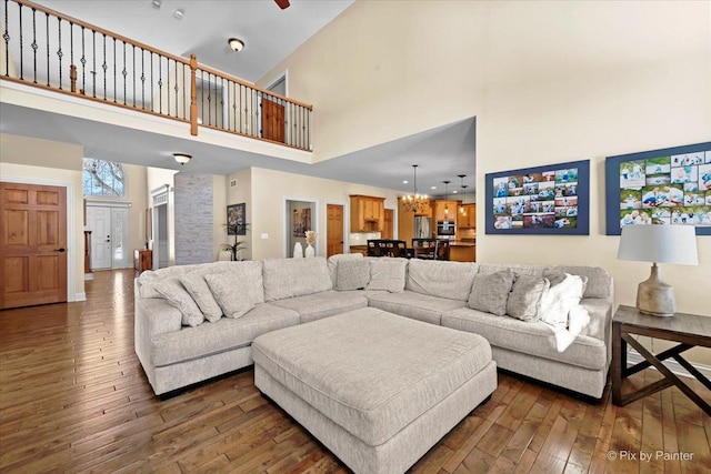 living area with a towering ceiling, dark wood-type flooring, and ceiling fan with notable chandelier