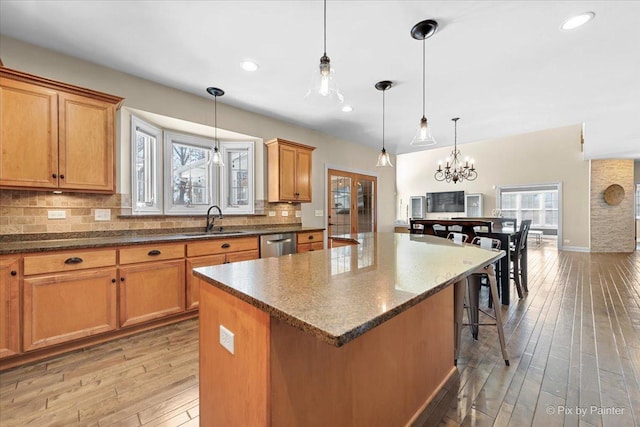 kitchen featuring decorative backsplash, a kitchen island, a sink, dishwasher, and a kitchen bar