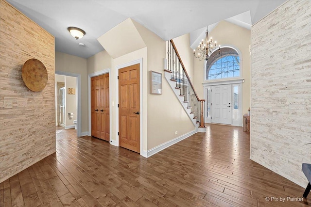 entrance foyer featuring a notable chandelier, a towering ceiling, dark wood-type flooring, baseboards, and stairs