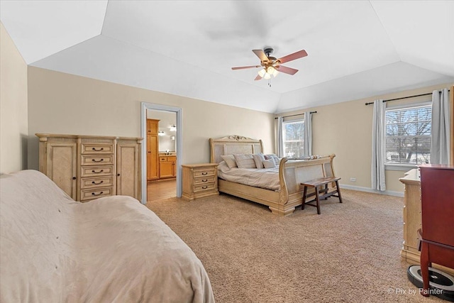 bedroom with connected bathroom, light carpet, baseboards, vaulted ceiling, and a tray ceiling