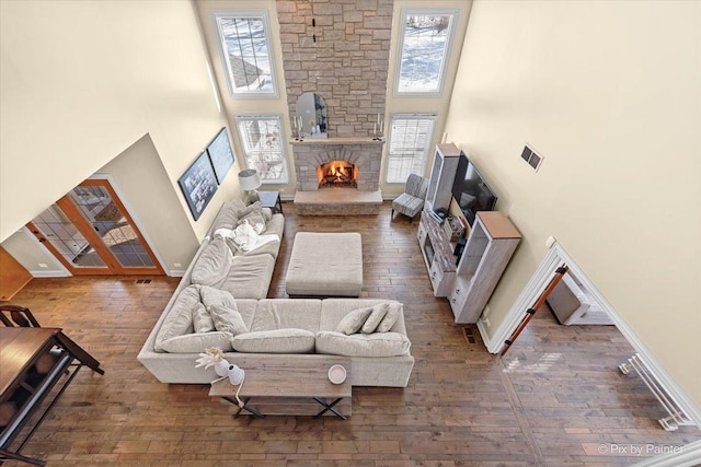 living area with a towering ceiling, baseboards, hardwood / wood-style floors, and a stone fireplace