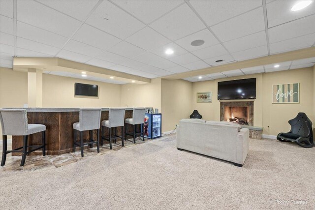 living room featuring carpet, a warm lit fireplace, baseboards, and a bar