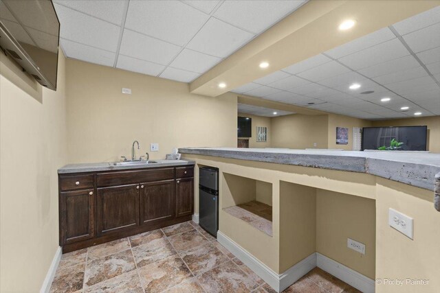 kitchen featuring a drop ceiling, dark brown cabinetry, a sink, baseboards, and light countertops