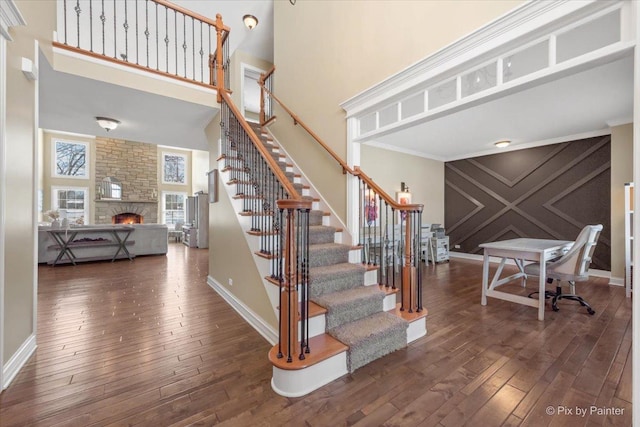 staircase with baseboards, wood-type flooring, ornamental molding, a high ceiling, and a fireplace