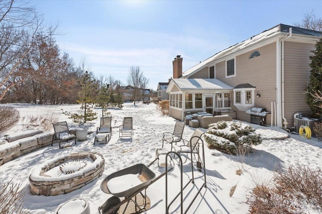 snow covered property featuring an outdoor fire pit, a chimney, cooling unit, and a sunroom