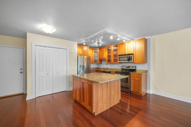 kitchen with light stone countertops, appliances with stainless steel finishes, a center island, and dark hardwood / wood-style floors