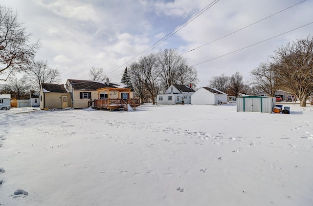 yard covered in snow featuring a wooden deck and a storage unit