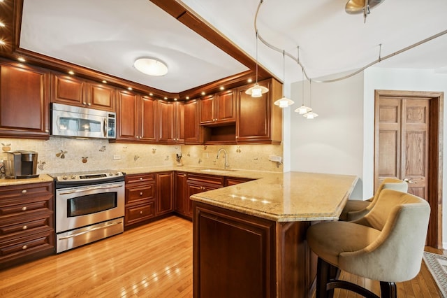 kitchen featuring a kitchen bar, sink, hanging light fixtures, appliances with stainless steel finishes, and kitchen peninsula