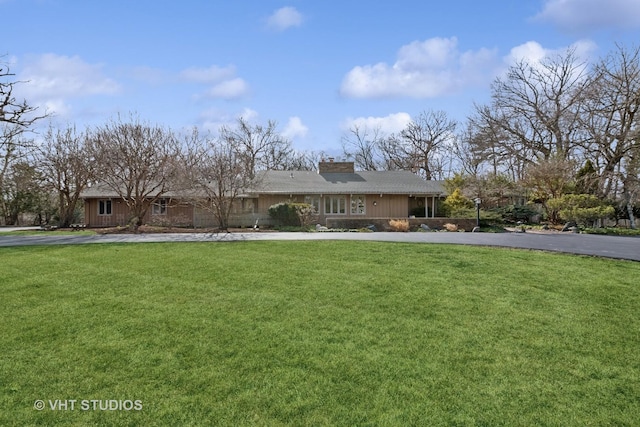 view of front facade featuring driveway, a chimney, and a front lawn