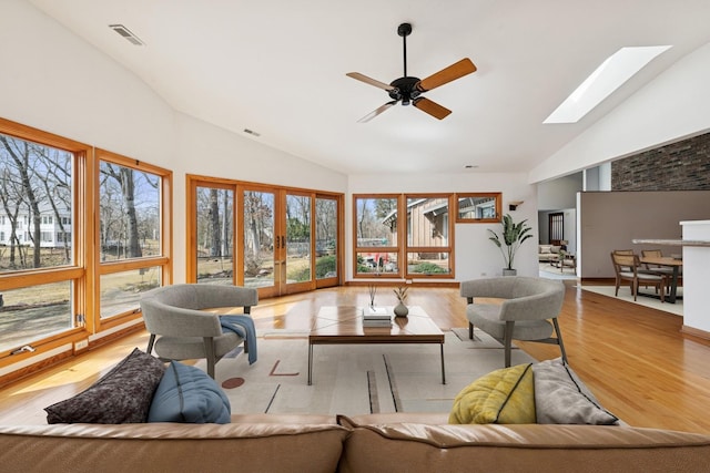 interior space featuring visible vents, light wood-style flooring, a skylight, high vaulted ceiling, and a ceiling fan