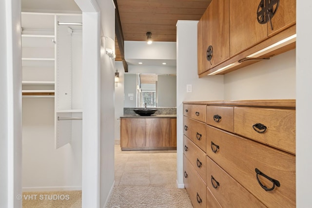 kitchen featuring brown cabinetry, light tile patterned flooring, a sink, wood ceiling, and light colored carpet