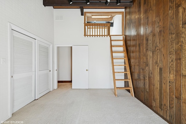 unfurnished bedroom with visible vents, a closet, carpet, wooden walls, and a towering ceiling