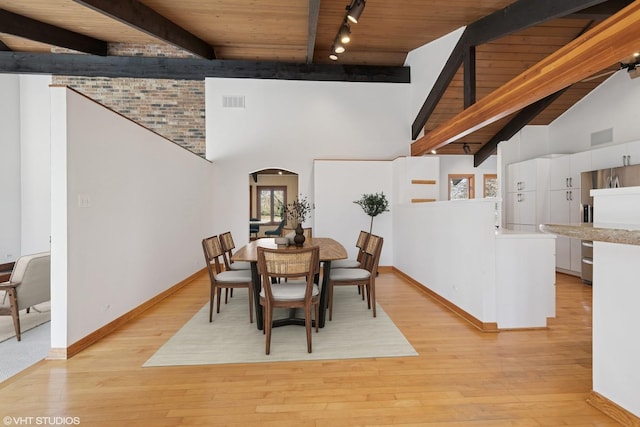 dining room with beamed ceiling, arched walkways, light wood-style flooring, and wooden ceiling