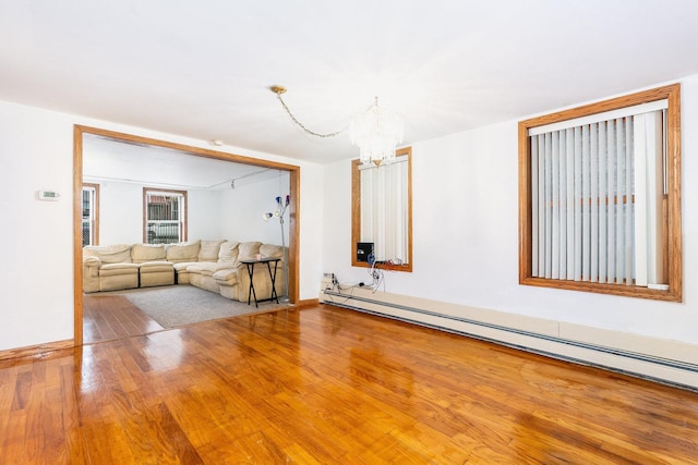 unfurnished living room featuring baseboard heating, wood-type flooring, and an inviting chandelier