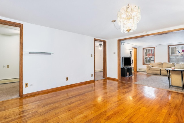 unfurnished living room featuring an inviting chandelier, a baseboard heating unit, and hardwood / wood-style flooring