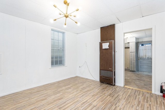 spare room with a drop ceiling, light hardwood / wood-style floors, and a notable chandelier