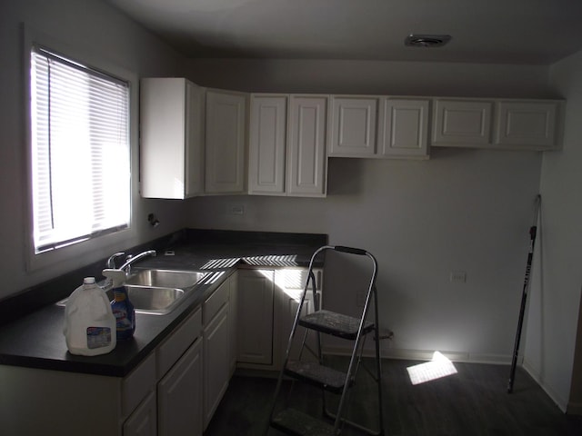 kitchen featuring dark countertops, white cabinets, a sink, and visible vents