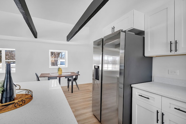 kitchen featuring beamed ceiling, stainless steel fridge, light wood-type flooring, and white cabinets