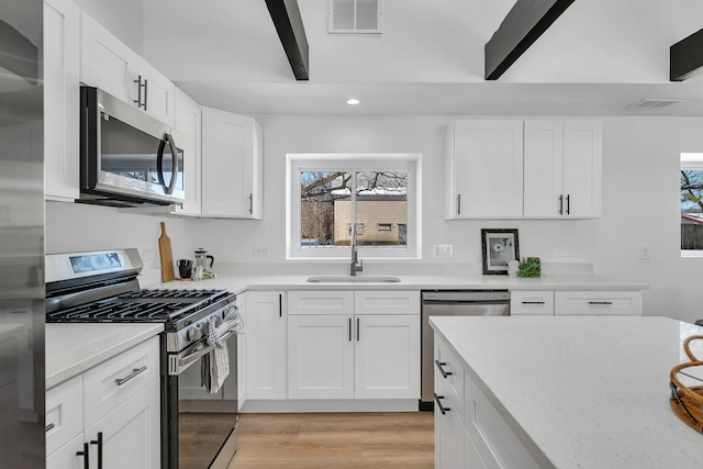 kitchen with sink, light hardwood / wood-style flooring, stainless steel appliances, light stone countertops, and white cabinets