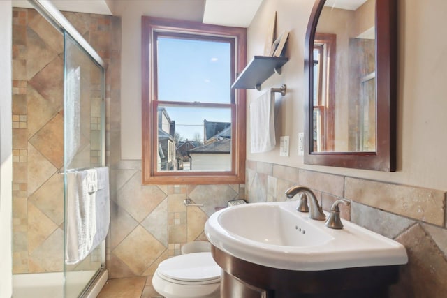 bathroom with toilet, a wainscoted wall, a sink, tile walls, and a shower stall