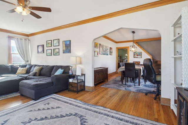 living area featuring arched walkways, ceiling fan, baseboards, hardwood / wood-style floors, and crown molding