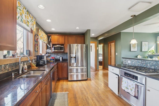 kitchen featuring a sink, appliances with stainless steel finishes, light wood-type flooring, dark stone countertops, and pendant lighting