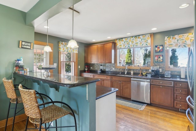 kitchen with dishwasher, brown cabinetry, a kitchen bar, and light wood-style floors