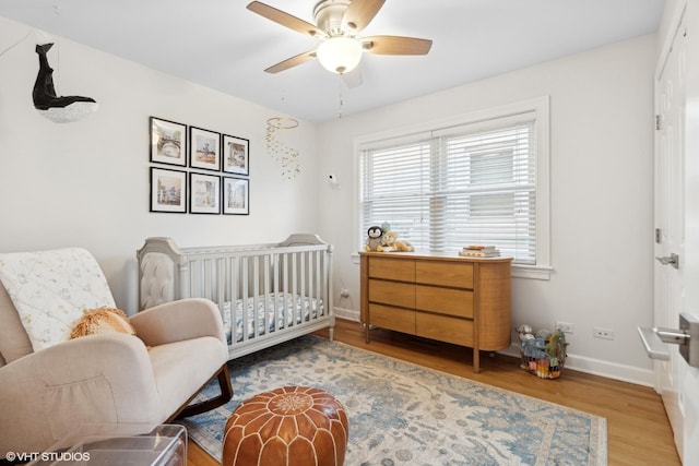 bedroom featuring light wood finished floors, a crib, a ceiling fan, and baseboards