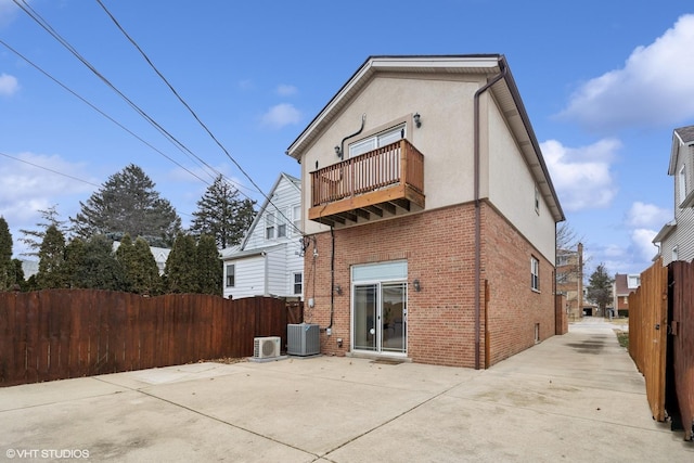 back of property with brick siding, stucco siding, central air condition unit, fence, and a balcony