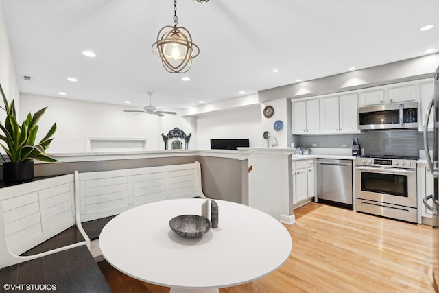 kitchen featuring decorative light fixtures, a peninsula, stainless steel appliances, light countertops, and white cabinetry