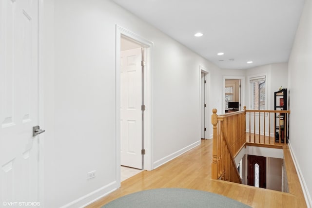 hallway featuring baseboards, wood finished floors, an upstairs landing, and recessed lighting